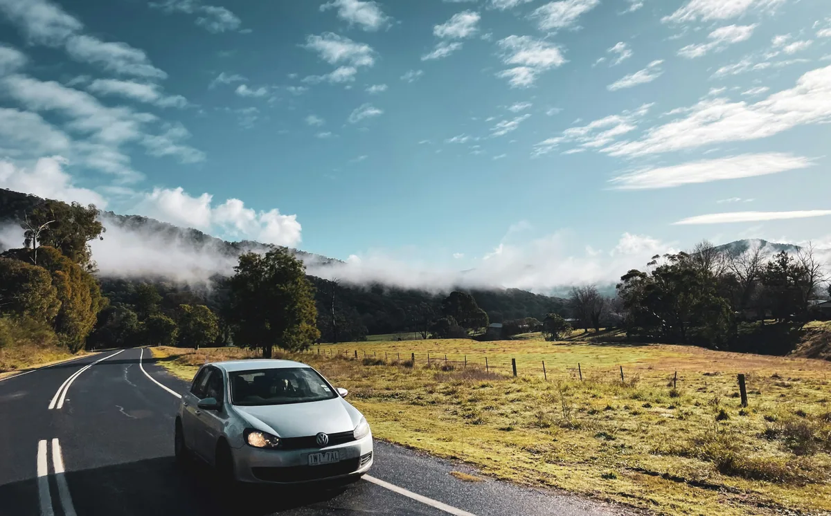 A car driving along a mountain road under low mist and bright morning light near Dinner Plain.