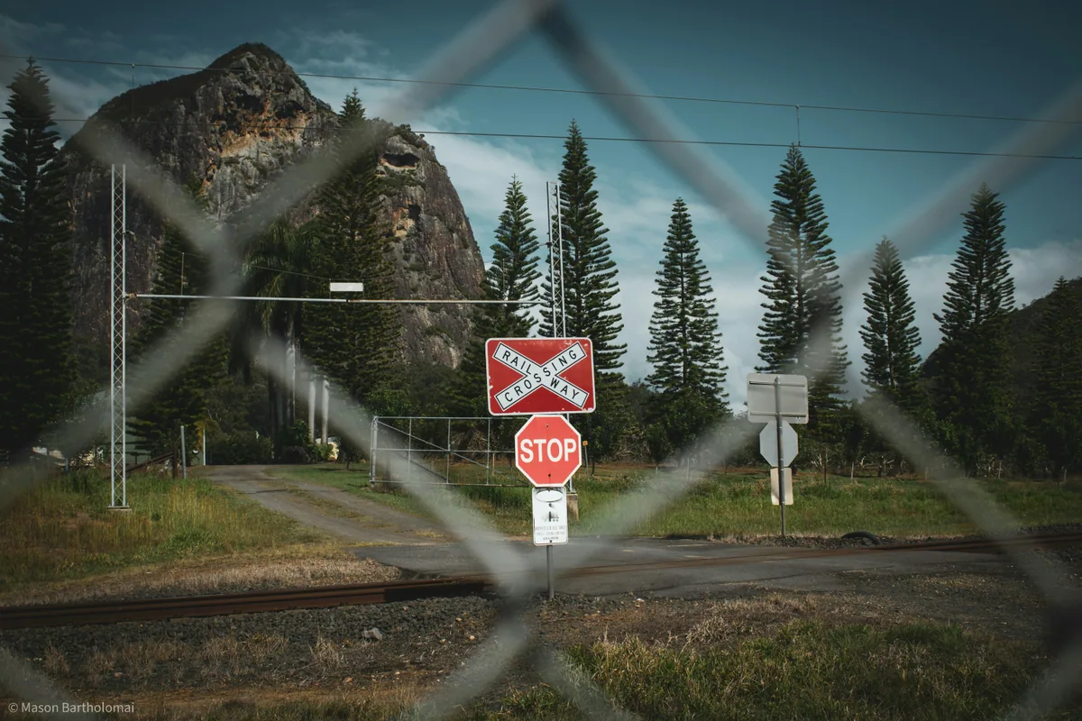 A railway stop sign seen through chain-link fence with the Glass House Mountains behind it.